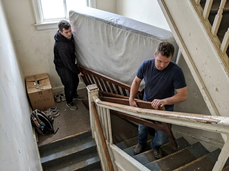 Crew carrying a bed frame down a narrow stairwell