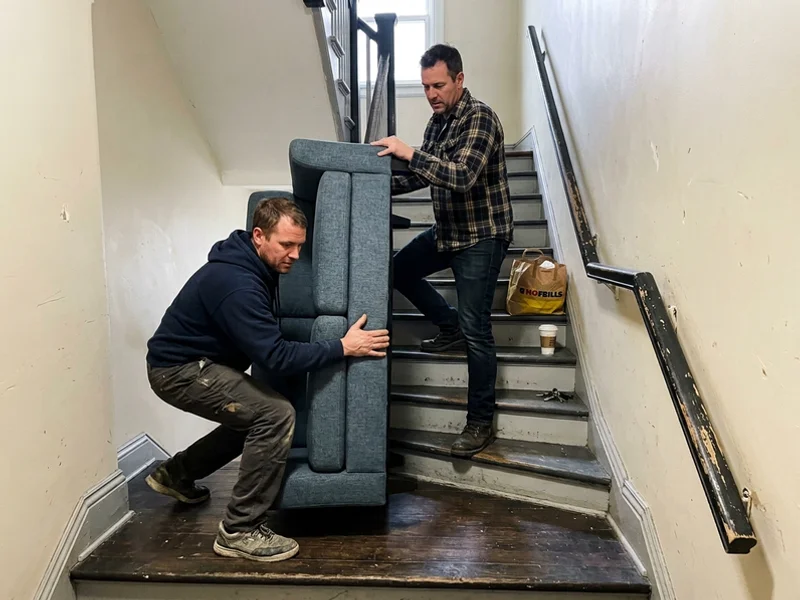 Crew navigating a loveseat down a tight stairwell